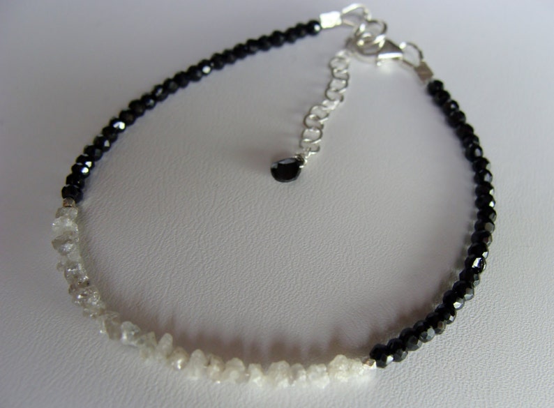 May include: A black and white beaded bracelet with a silver clasp. One half of the bracelet is made of black beads, and the other half is made of white beads.