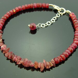 May include: A red gemstone bracelet with a silver clasp. The bracelet is made of small, faceted gemstones that are strung together on a silver chain.