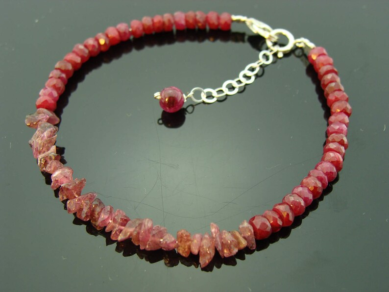 May include: A red gemstone bracelet with a silver clasp. The bracelet is made of small, faceted gemstones that are strung together on a silver chain.