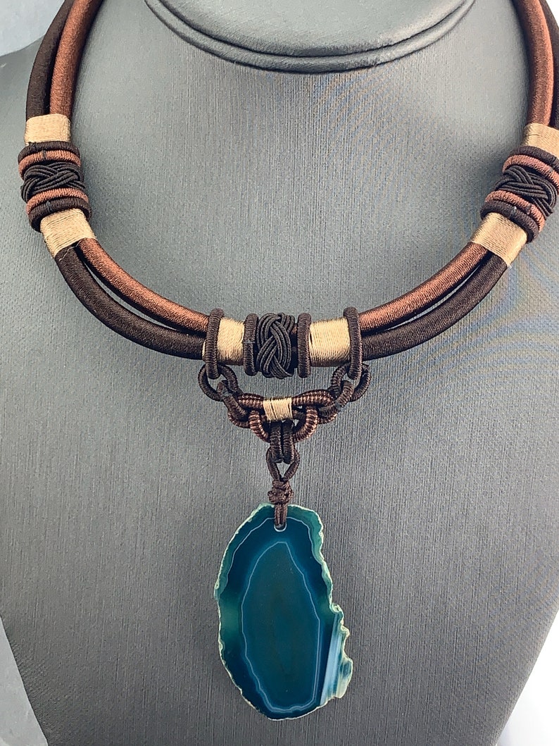 Pu&ograve; includere: Una collana di corda intrecciata marrone e beige con un ciondolo in agata verde. Il ciondolo &egrave; una pietra naturale con un motivo unico.