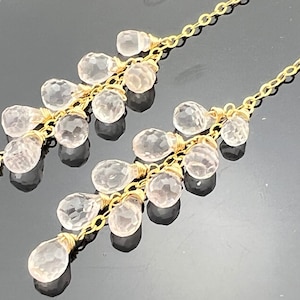 Pu&ograve; includere: Un paio di orecchini pendenti in oro con pi&ugrave; cristalli trasparenti a forma di goccia.