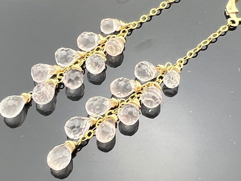 Pu&ograve; includere: Un paio di orecchini pendenti in oro con pi&ugrave; cristalli trasparenti a forma di goccia.
