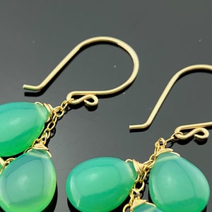 May include: A pair of gold dangle earrings with green gemstone drops. The earrings feature a delicate chain and multiple teardrop-shaped stones.