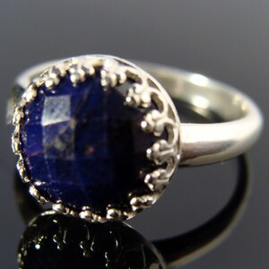 May include: A silver ring with a dark blue gemstone set in a decorative silver bezel. The ring has a simple band.