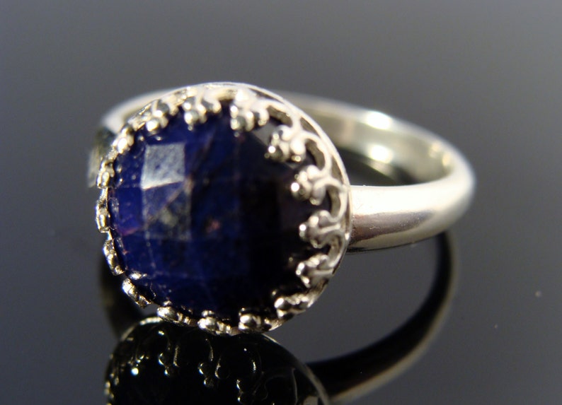 May include: A silver ring with a dark blue gemstone set in a decorative silver bezel. The ring has a simple band.
