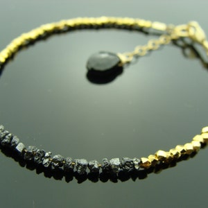 May include: A black diamond bracelet with gold beads. The bracelet has a black diamond charm.