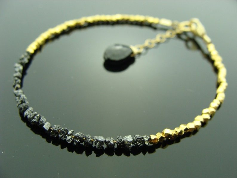May include: A black diamond bracelet with gold beads. The bracelet has a black diamond charm.
