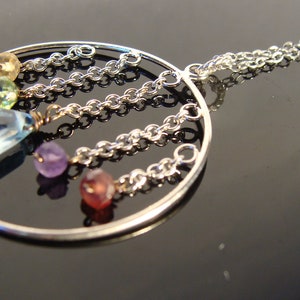 May include: A silver necklace with a circular pendant featuring a variety of colourful gemstones, including blue, green, pink, and purple.