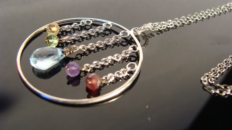 May include: A silver necklace with a circular pendant featuring a variety of colourful gemstones, including blue, green, pink, and purple.