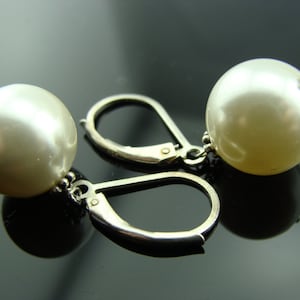 Puede incluir: Un par de pendientes de plata con bolas blancas nacaradas que cuelgan de la parte inferior. Los pendientes tienen un cierre de palanca.