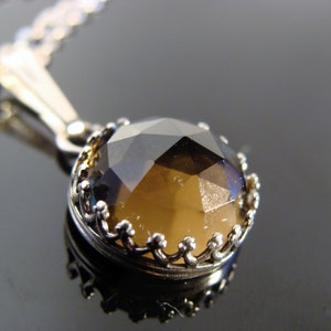 May include: A silver pendant necklace featuring a faceted, round, smoky quartz gemstone. The gemstone is set in a decorative, crown-like bezel. The chain is delicate and silver, creating an elegant and classic jewelry piece.