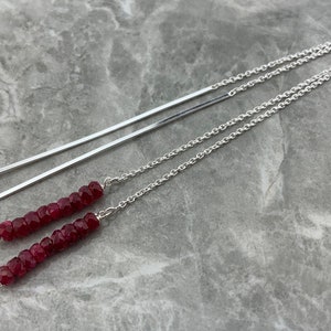 May include: A pair of long silver earrings with a chain and a bar, each with a strand of dark red gemstone beads.