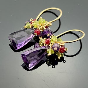 Könnte beinhalten: Amethyst-Ohrringe mit einem Cluster aus grünen, violetten und roten Edelsteinen. Die Ohrringe sind aus Gold.