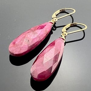 May include: A pair of gold earrings with pink teardrop-shaped gemstones. The earrings have a simple design and are perfect for everyday wear.