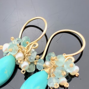 Op de afbeelding: Gouden oorbellen met turquoise en aquamarijn stenen. De oorbellen zijn gemaakt met draadgewikkelde stenen en hebben een hangend ontwerp.