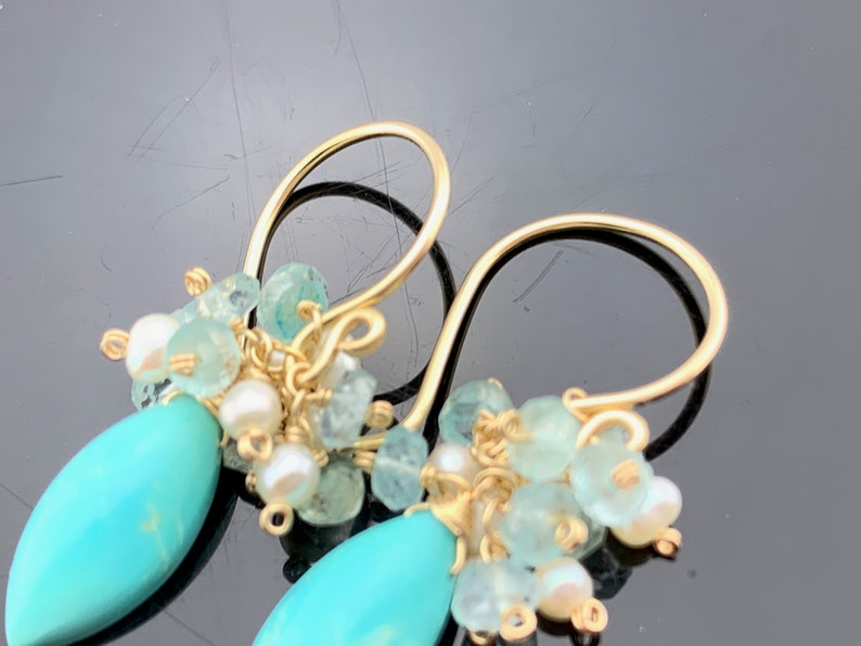 Op de afbeelding: Gouden oorbellen met turquoise en aquamarijn stenen. De oorbellen zijn gemaakt met draadgewikkelde stenen en hebben een hangend ontwerp.