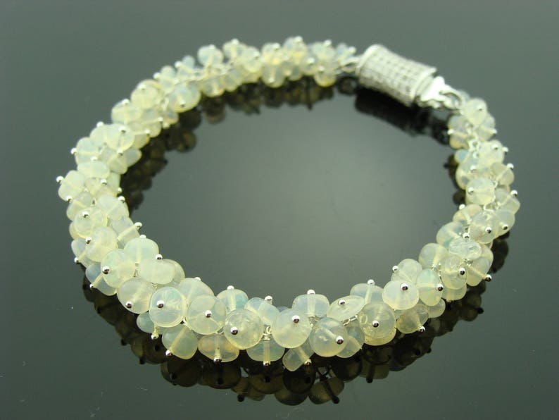 May include: A silver bracelet with a clasp closure, featuring a cluster of white opal beads.