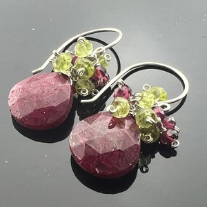 以下が含まれることがあります： 大きなファセットカットの赤い宝石と、より小さな緑と赤の宝石のクラスターが付いた、ぶら下がりのイヤリングのペアです。