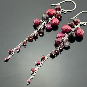 Op de afbeelding: Een paar oorhangers met een zilveren ketting en meerdere rode en paarse edelstenen.