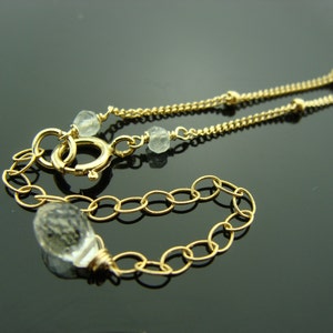 May include: A gold chain necklace with clear faceted gemstone beads. The necklace has a lobster clasp closure.
