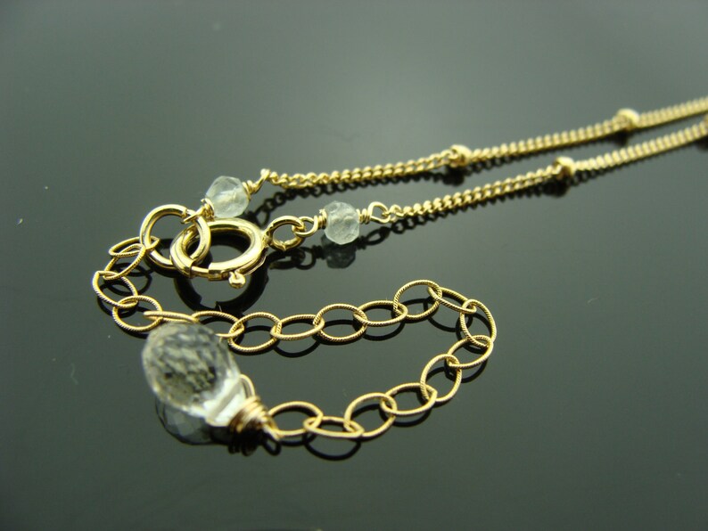 May include: A gold chain necklace with clear faceted gemstone beads. The necklace has a lobster clasp closure.