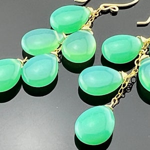 May include: A pair of green gemstone dangle earrings with gold chain links. The earrings feature multiple teardrop-shaped gemstones.