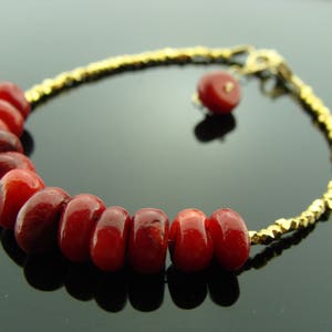 Op de afbeelding: Een gouden kettingarmband met rode koraal kralen. De armband heeft een klein gouden bedeltje.
