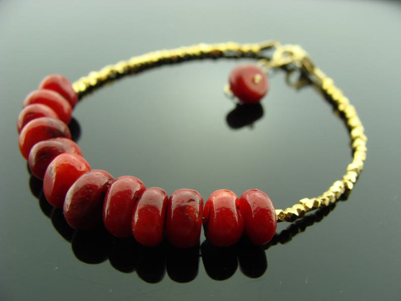 Op de afbeelding: Een gouden kettingarmband met rode koraal kralen. De armband heeft een klein gouden bedeltje.