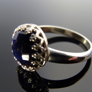 May include: A silver ring with a dark blue gemstone set in a decorative filigree design.
