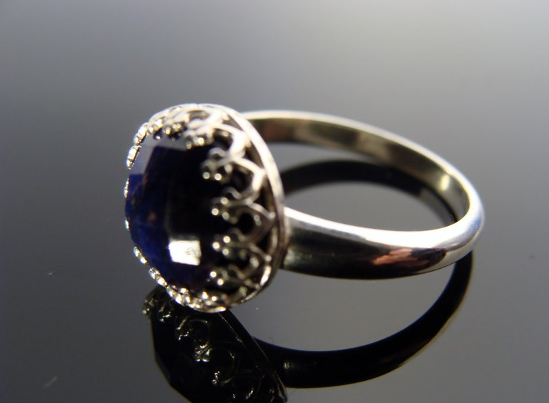 May include: A silver ring with a dark blue gemstone set in a decorative filigree design.