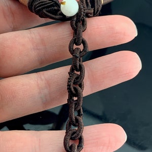 Pu&ograve; includere: Una collana di corda marrone con un ciondolo bianco e un'estensione a catena marrone.