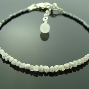 May include: A silver bracelet featuring a row of rough white diamonds and a row of black beads. The bracelet has a silver clasp and a small silver charm.