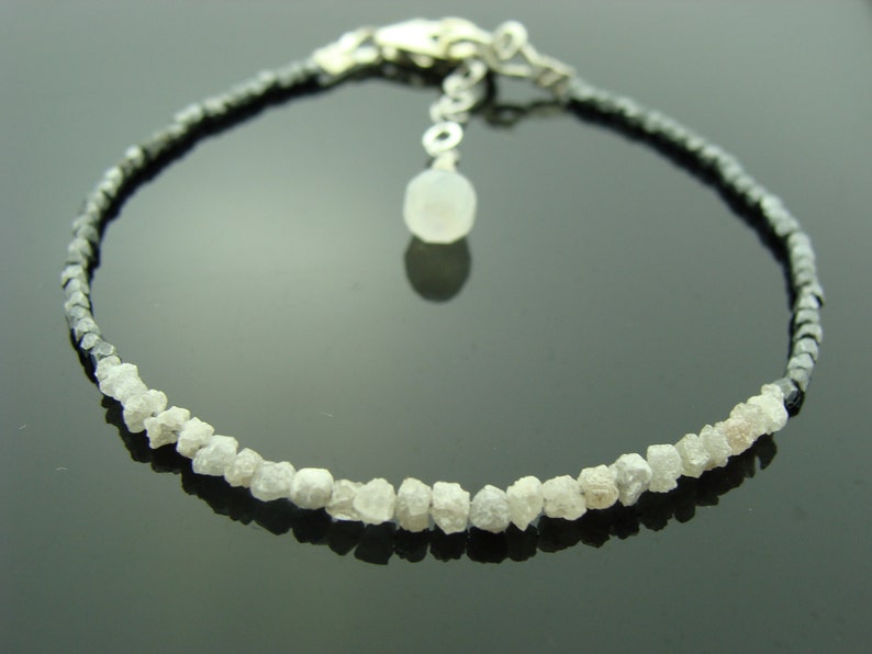 May include: A silver bracelet featuring a row of rough white diamonds and a row of black beads. The bracelet has a silver clasp and a small silver charm.