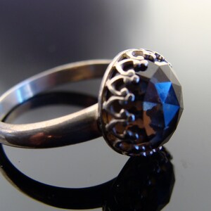 Puede incluir: Un anillo de plata con una gran piedra preciosa facetada de color azul oscuro engastada en una corona de plata decorativa.