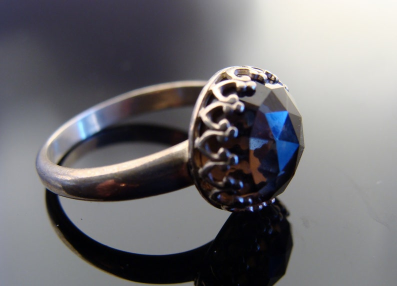 Puede incluir: Un anillo de plata con una gran piedra preciosa facetada de color azul oscuro engastada en una corona de plata decorativa.