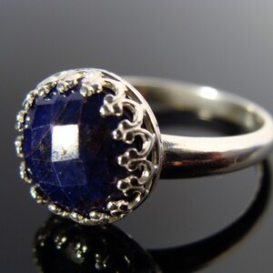 May include: A silver ring with a dark blue gemstone set in a filigree design.