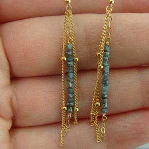 Puede incluir: Un par de pendientes de oro con m&uacute;ltiples cadenas y detalles de diamantes azules.