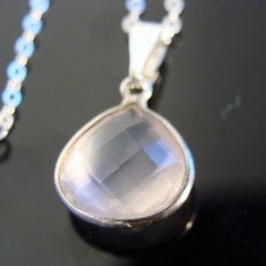 May include: A silver chain necklace with a teardrop-shaped pendant featuring a clear, faceted rose quartz stone.