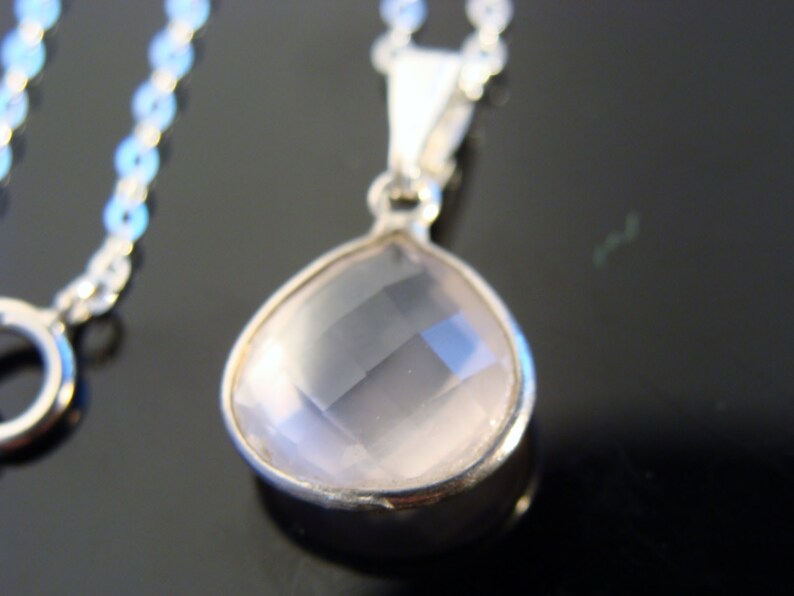 May include: A silver chain necklace with a teardrop-shaped pendant featuring a clear, faceted rose quartz stone.