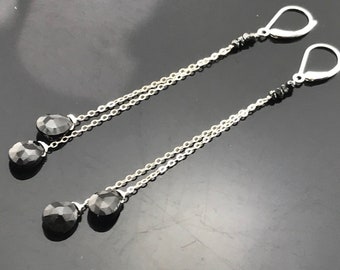 May include: A pair of silver dangle earrings with black teardrop-shaped gemstones. The earrings have a delicate chain design and are perfect for adding a touch of elegance to any outfit.