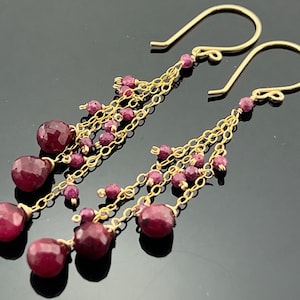 May include: Gold earrings with multiple strands of chain and dangling ruby red gemstones.