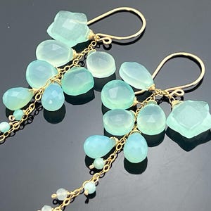 May include: A pair of gold-tone earrings featuring clusters of light blue and green gemstones. The earrings have a delicate chain design with various shapes of gemstones, including teardrops and irregular shapes.