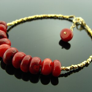 Op de afbeelding: Een gouden kettingarmband met rode koraal kralen. De armband heeft een klein gouden bedeltje.