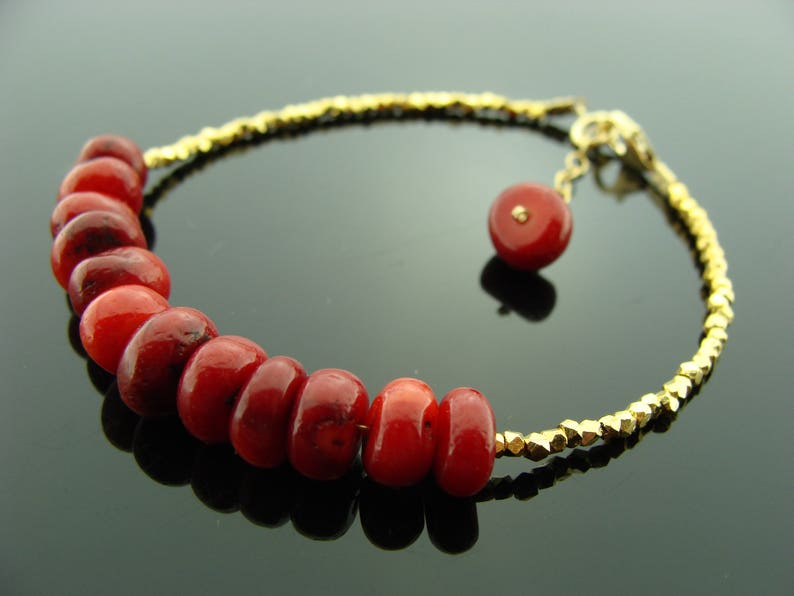 Op de afbeelding: Een gouden kettingarmband met rode koraal kralen. De armband heeft een klein gouden bedeltje.
