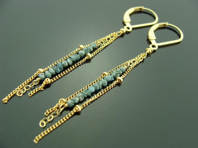 Puede incluir: Un par de pendientes de oro con un dise&ntilde;o de cadena colgante. Cada pendiente presenta m&uacute;ltiples hebras de cadena con peque&ntilde;as piedras preciosas azules talladas en bruto.