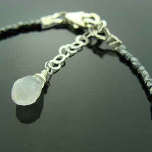 May include: A silver chain bracelet with a small, white gemstone pendant. The bracelet is made of faceted, black beads.