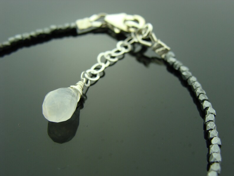 May include: A silver chain bracelet with a small, white gemstone pendant. The bracelet is made of faceted, black beads.
