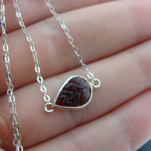 Puede incluir: Un collar de cadena de plata con un colgante en forma de l&aacute;grima que presenta un dise&ntilde;o de hoja tallada en un color burdeos oscuro.