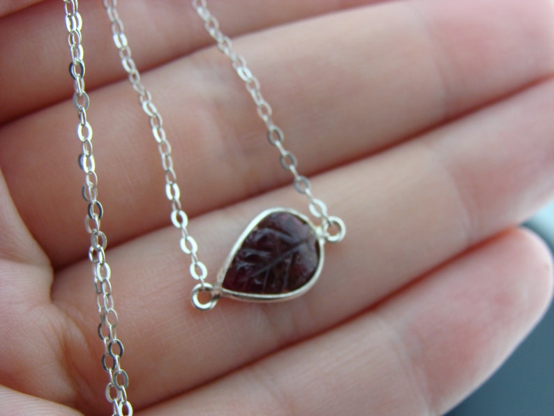 Puede incluir: Un collar de cadena de plata con un colgante en forma de l&aacute;grima que presenta un dise&ntilde;o de hoja tallada en un color burdeos oscuro.