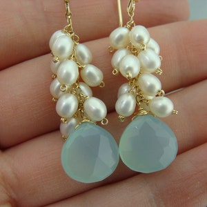 May include: A pair of dangle earrings with a light blue gemstone and a cluster of white pearls hanging from a gold wire.